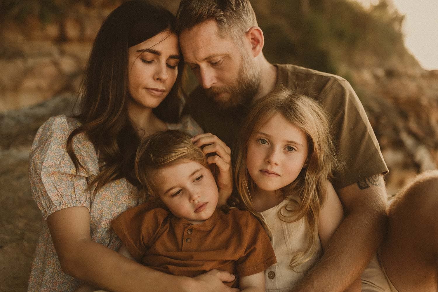 Family-photography-sydney-family-embrace-in-a-tender-moment-with-mum-lovingly-stroking-hair-of-young-boy-whilst-leaning-into-dad-and-little-girl-who-looks-directly-into-camera