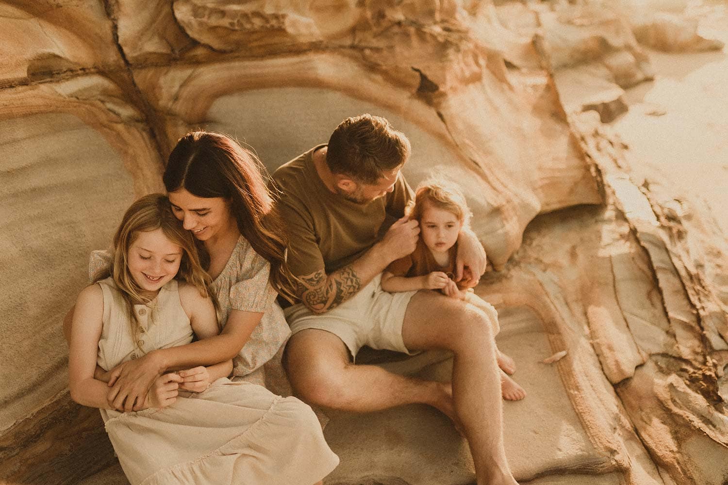 Lifestyle-family-photography-sydney-family-cuddling-on-rocks-in-the-sun
