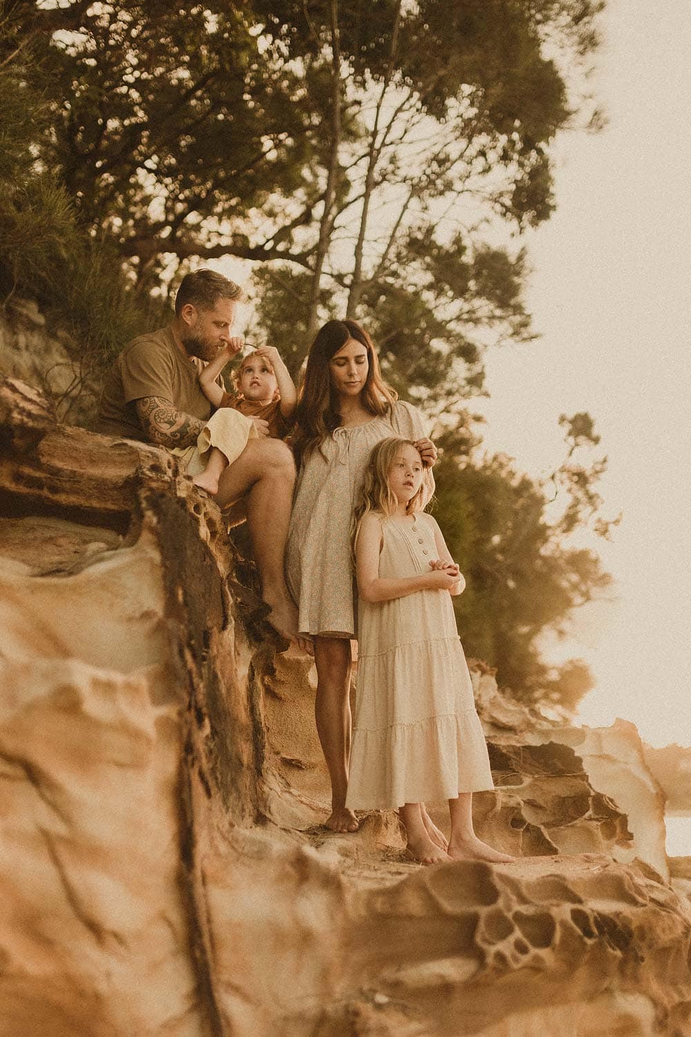 Sutherland-shire-family-lifestyle-photography-family-resting-on-rocks-whilst-mother-strokes-daughters-hair-and-little-boy-sits-on-dads-lap-as-he-animatedly-tells-story