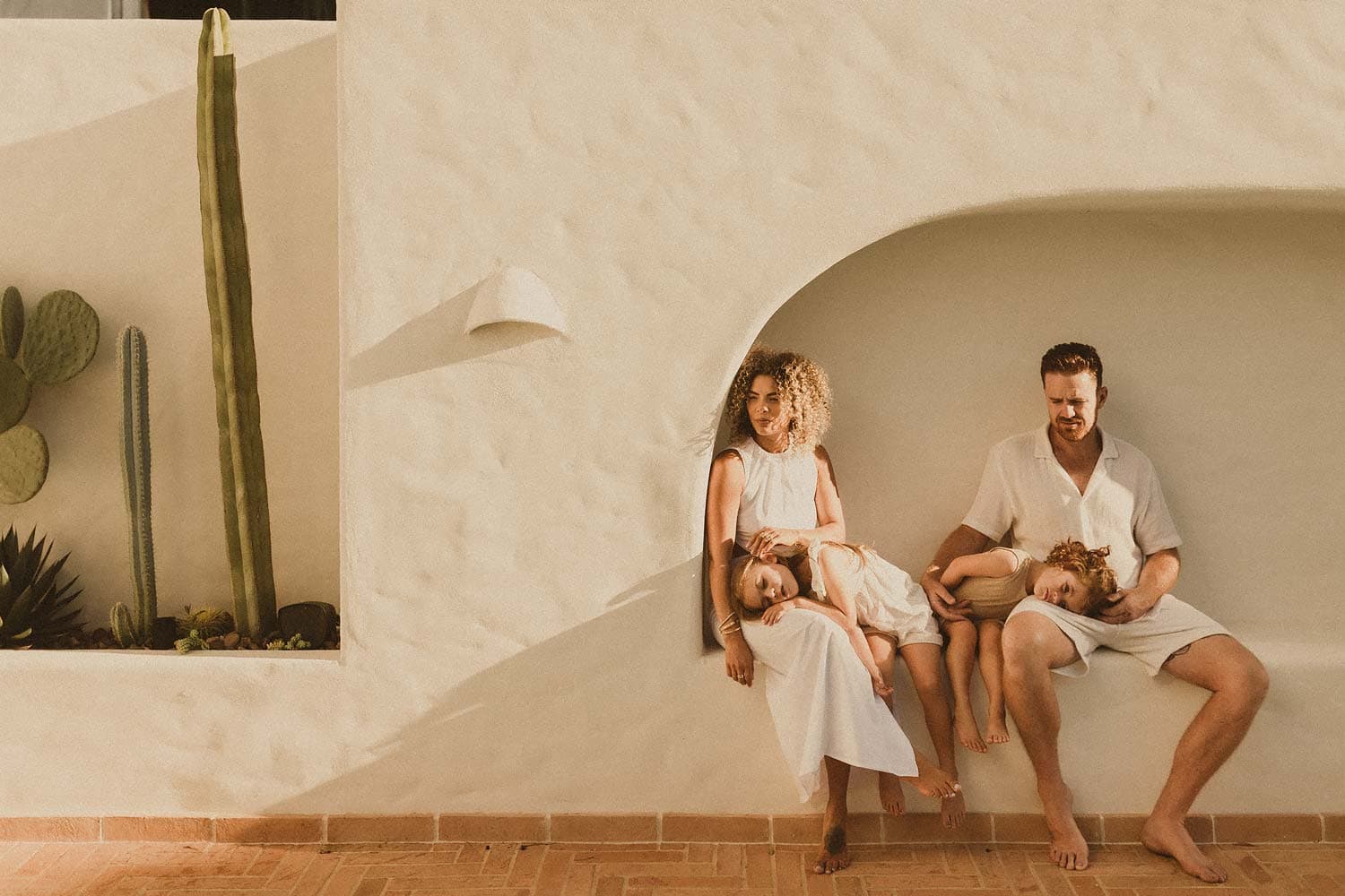 Sutherland-shire-family-photographer-mum-dad-and-young-children-dressed-in-neutrals-enjoy-the-dappled-afternoon-sun-in-very-european-inspired-nook-of-their-home-with-an-artsy-cactus-garden-beside-them