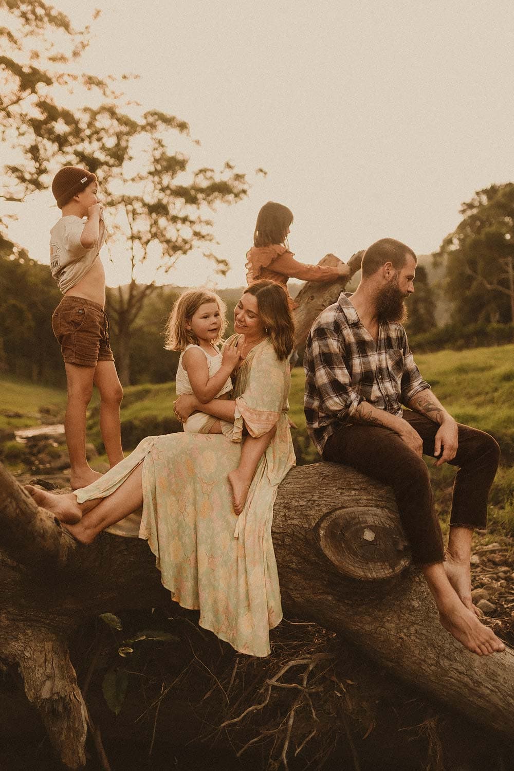 Sutherland-shire-family-photographer-family-on-fallen-tree-with-mum-and-daughter-sharing-moment-as-older-siblings-explore-and-play