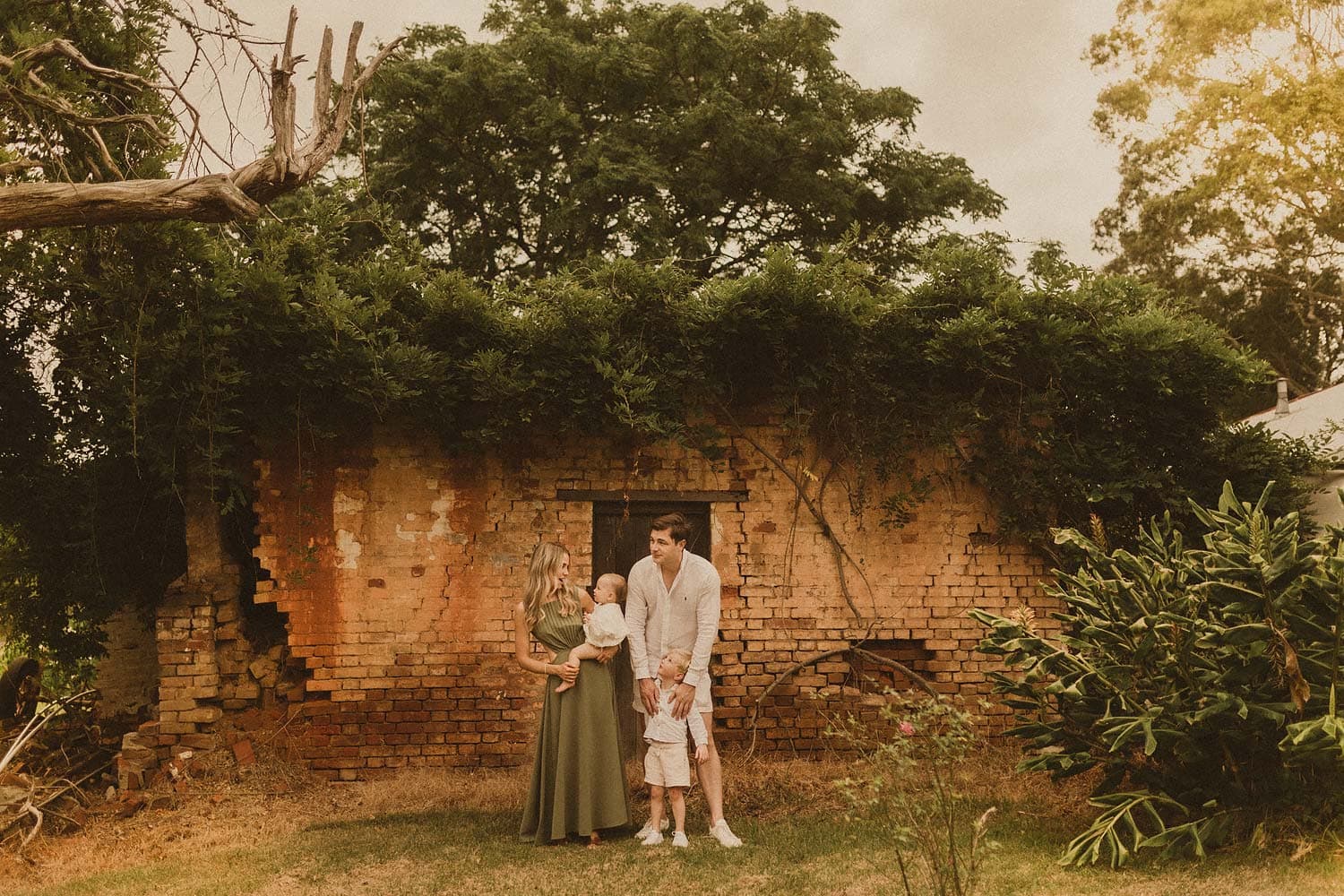 Sydney-family-photographer-family-infront-of-old-brick-buildong-that-is-starting-to-fall-down-mum-talking-to-baby