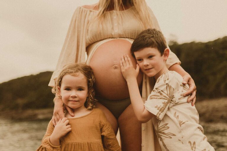 Close-up of pregnant belly, with son and daughter on either side, hands gently resting on a baby bump.