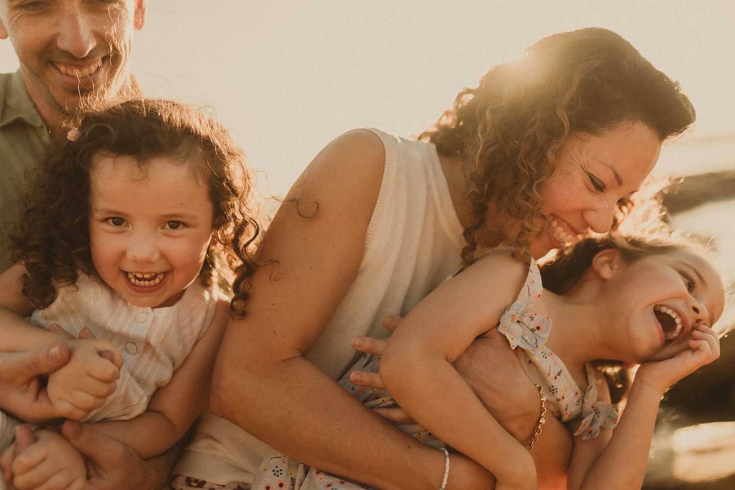 Mum laughing with her two daughters during a playful family photography session by the coast